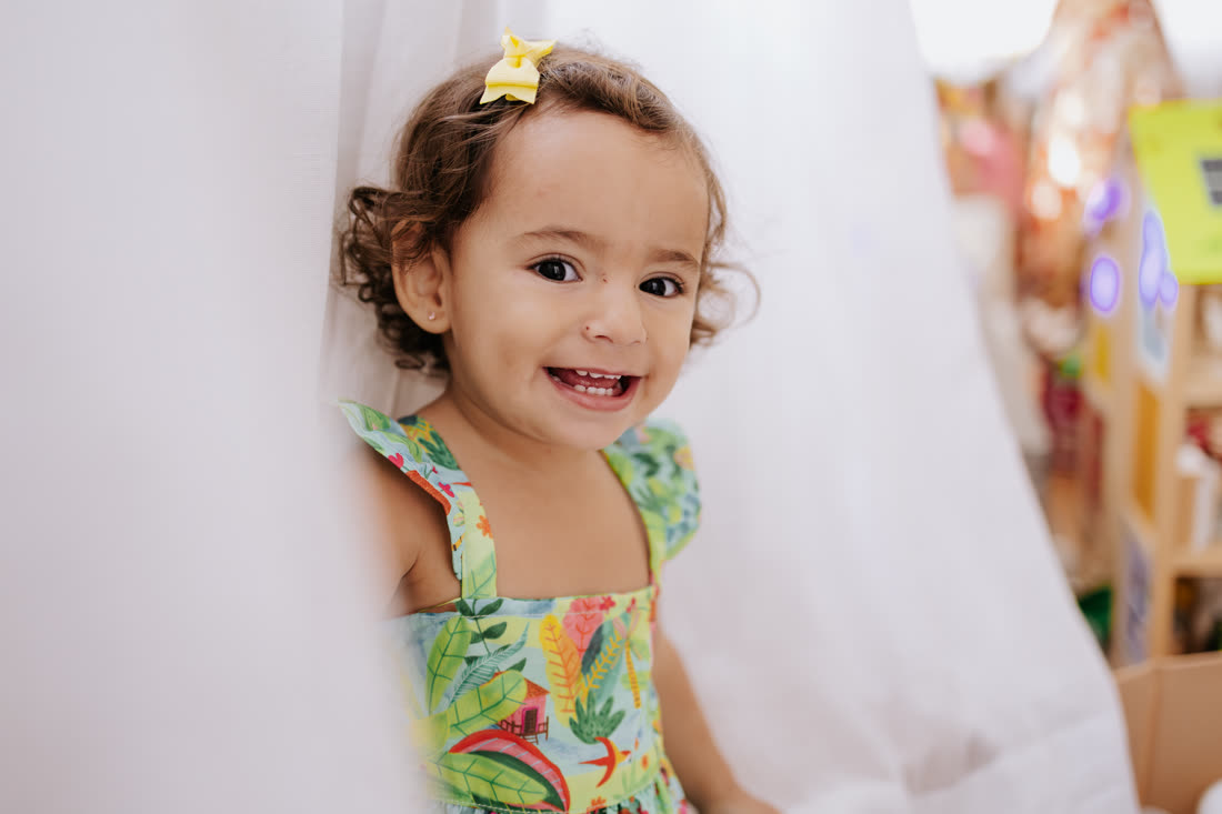 Menina sorrindo entre as cortinas brancas