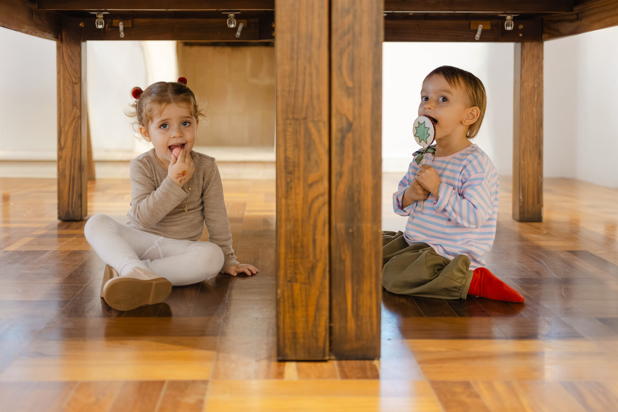 Duas crianças comendo doces sentadas embaixo da mesa