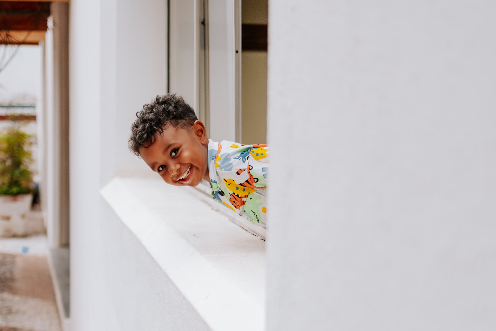 Menino sorrindo espiando pela janela de casa